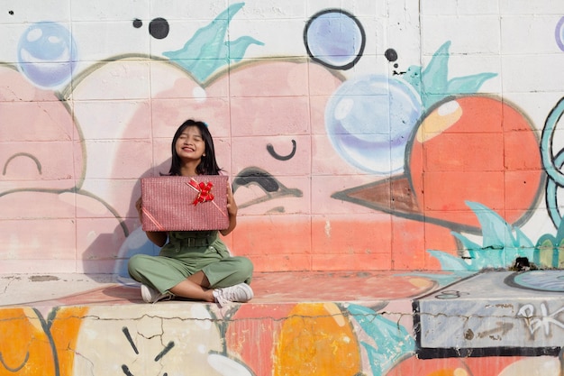 La joyeuse fille portant un chapeau de fête avec une boîte-cadeau assise sur un fond coloré