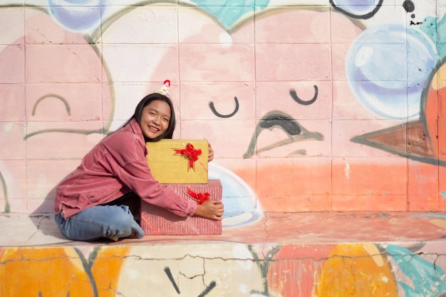 La joyeuse fille portant un chapeau de fête avec une boîte-cadeau assise sur un fond coloré