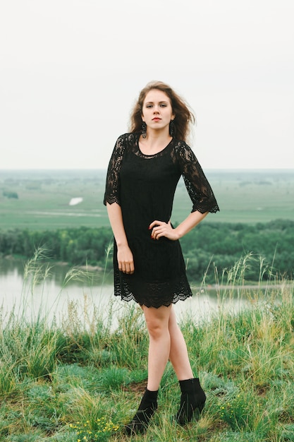 Joyeuse fille en robe de dentelle noire danse dans un pré sur la colline au-dessus de la rivière