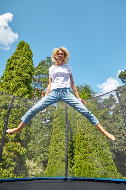 Joyeuse fille sautant sur un trampoline dans le parc. Vacances en ville, activités de plein air.