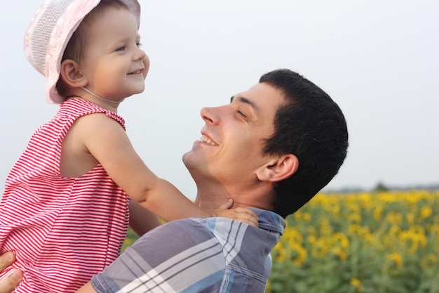 Photo joyeuse heureuse charmante cue fille bébé dans le sourire père mains appréciant la nature se promener dans les tournesols prairie famille célébrant la fête des pères ensemble