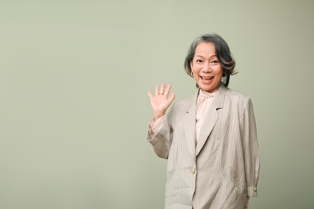 Joyeuse et heureuse femme d'affaires âgée asiatique souriante agitant la main fond isolé Bonjour au revoir