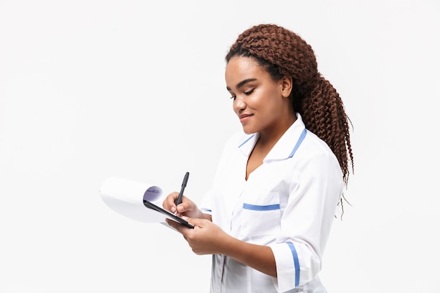 joyeuse infirmière écrivant un rapport de cas médical isolé contre un mur blanc