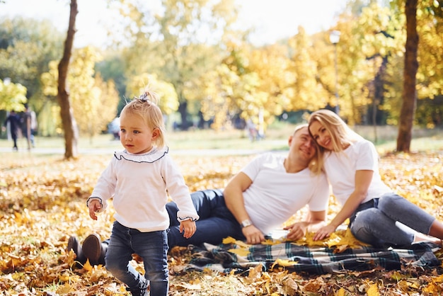 Joyeuse jeune famille allongée sur le sol et se reposer ensemble dans un parc d'automne.