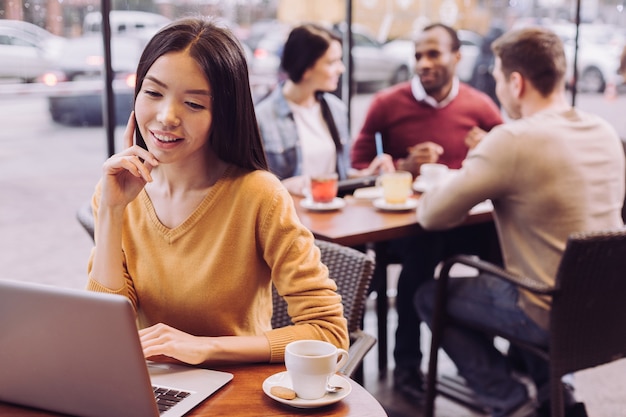 Joyeuse jeune femme agréable se détendre au café tout en souriant et en touchant son visage