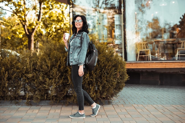 Joyeuse jeune femme appréciant une boisson chaude dans la rue