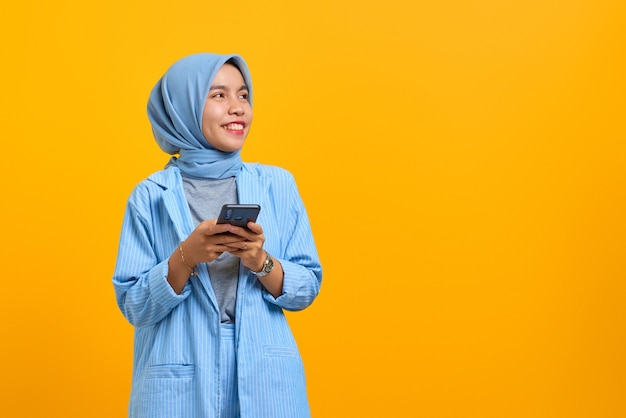 Joyeuse jeune femme asiatique utilisant un téléphone portable et regardant de côté un espace vide