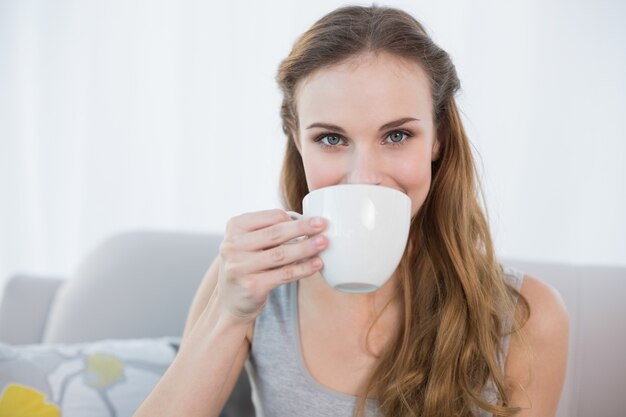 Joyeuse jeune femme assise sur le canapé tenant la tasse