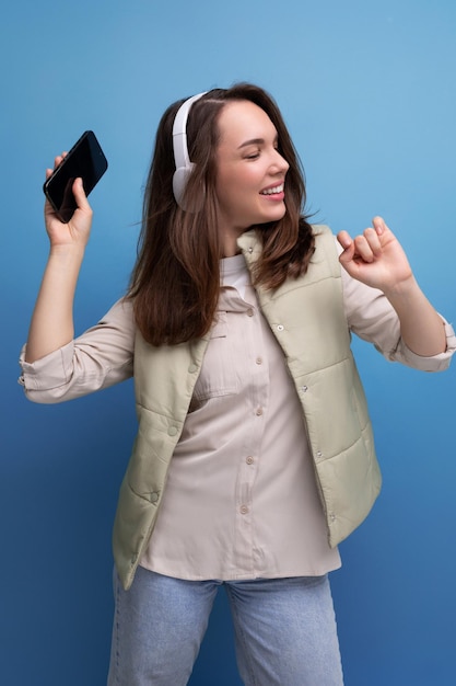 Joyeuse jeune femme brune danse en écoutant de la musique dans des écouteurs sur un fond de studio