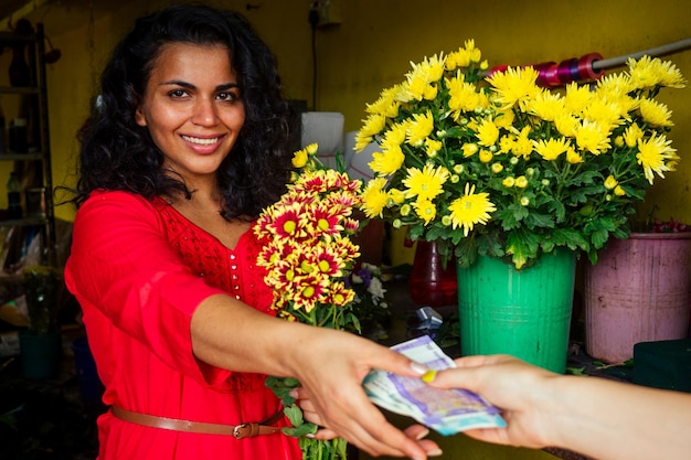 Joyeuse jeune femme brune fleuriste vendant des fleurs dans un magasin de fleurs prenant de l'argent du client