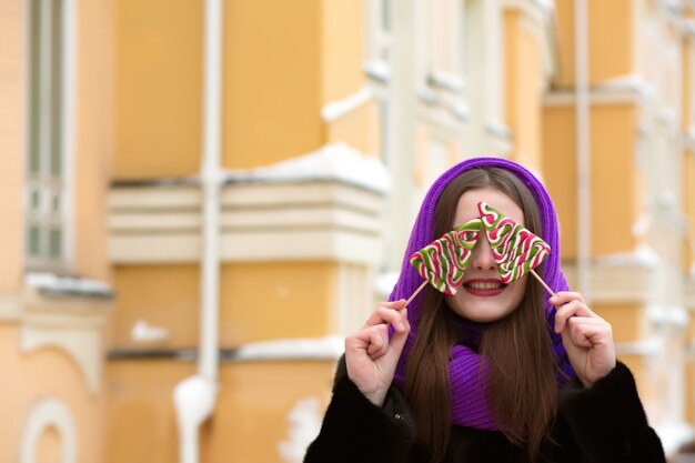 Joyeuse jeune femme brune en foulard violet s'amusant avec les bonbons de Noël colorés