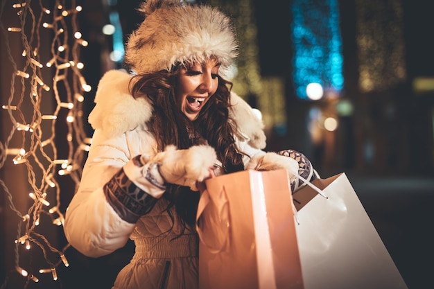 Photo joyeuse jeune femme avec cadeau s'amusant dans la rue de la ville à l'époque de noël.