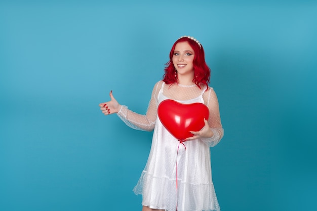 joyeuse jeune femme dans une robe blanche tient un ballon volant en forme de coeur et donne un coup de pouce