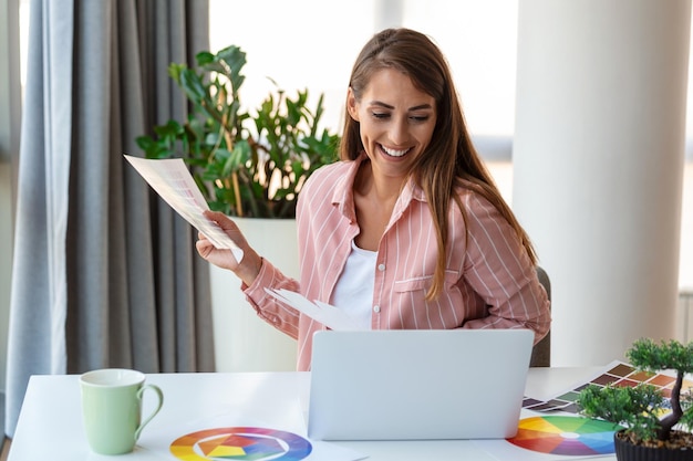 Joyeuse jeune femme designer ayant une vidéoconférence avec des clients assis au bureau devant un ordinateur tenant des palettes de couleurs gesticulant et souriant copie espace