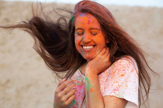 Joyeuse jeune femme avec du vent dans les cheveux célébrant le festival des couleurs Holi dans le désert. Espace pour le texte