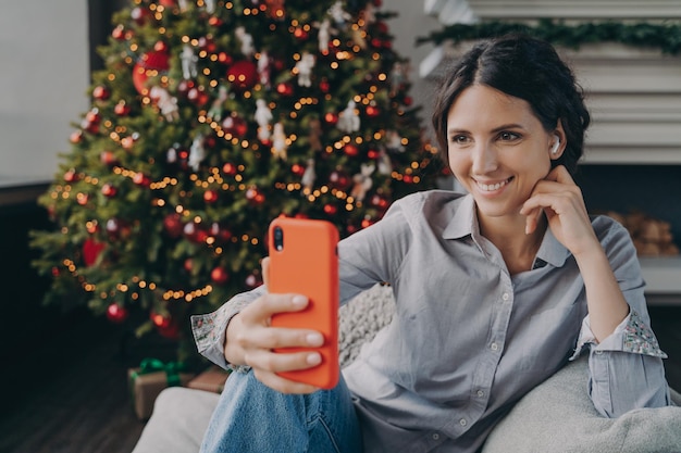 Joyeuse jeune femme espagnole profitant de la période de Noël à la maison en faisant un selfie sur un smartphone