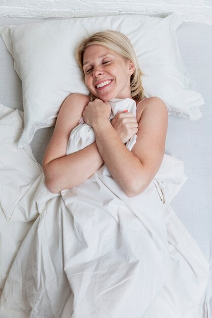 Joyeuse jeune femme est allongée dans son lit. Sommeil complet et détente.