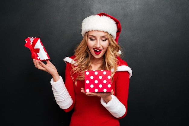 Joyeuse jeune femme excitée en costume de père Noël ouvrant la boîte présente