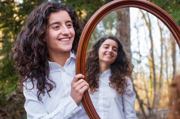 Joyeuse jeune femme montrant le reflet dans un miroir de soeur jumelle dans la forêt