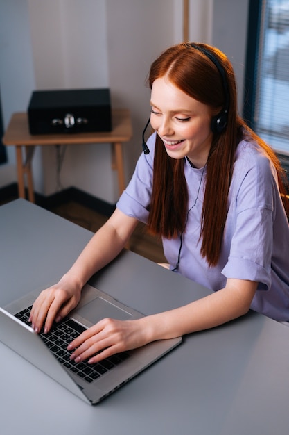 joyeuse jeune femme opératrice utilisant un casque et un ordinateur portable pendant le support client au bureau à domicile