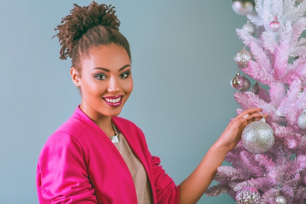 joyeuse jeune femme rase mixte en veste fuchsia élégante près de l'arbre de noël