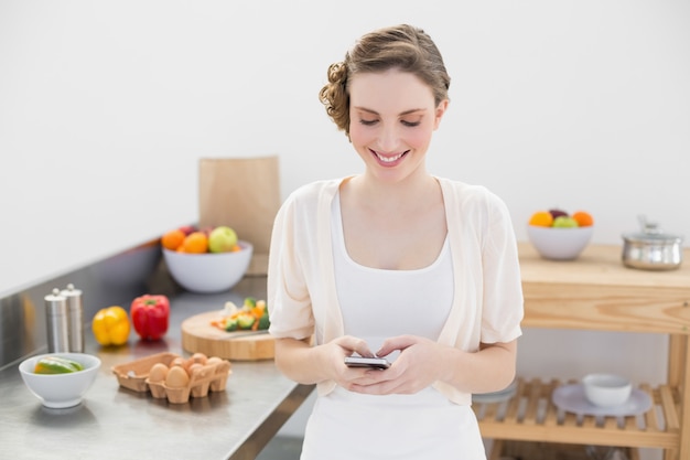 Joyeuse jeune femme avec son smartphone debout dans la cuisine