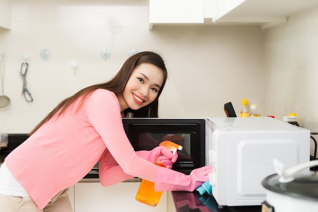 Joyeuse jeune femme souriante en tablier de nettoyage dans la cuisine domestique avec pulvérisateur