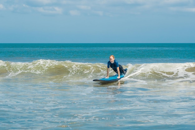 Joyeuse jeune femme surfeuse débutante au surf bleu s'amuse sur les petites vagues de la mer. Mode de vie familial actif, cours de sports nautiques en plein air et activité de natation pendant les vacances d'été du camp de surf.