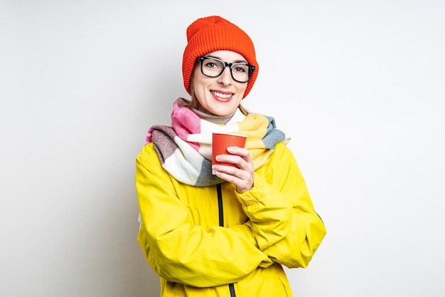 Joyeuse jeune femme en veste jaune avec gobelet en papier sur fond clair.