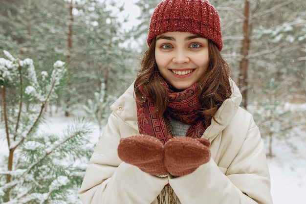 joyeuse jeune femme en vêtements d'extérieur et neige sur des mitaines tricotées regardant la caméra dans la forêt d'hiver