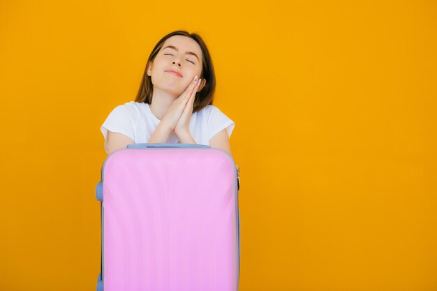 joyeuse jeune femme vêtue de vêtements d'été et de lunettes de soleil debout avec une valise