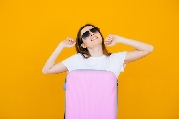 joyeuse jeune femme vêtue de vêtements d'été et de lunettes de soleil debout avec une valise