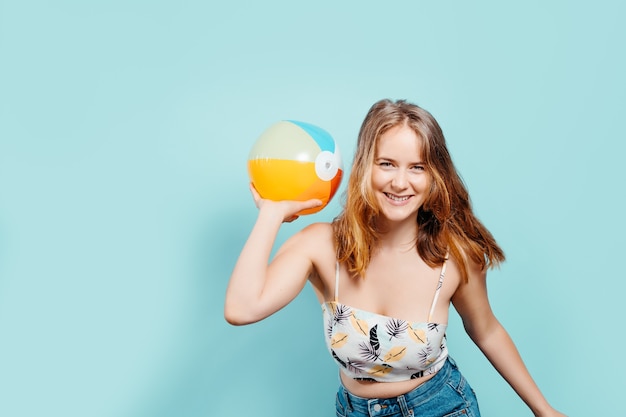 Joyeuse jeune fille blonde regardant la caméra tenant un ballon gonflable portant un haut d'été sur fond bleu