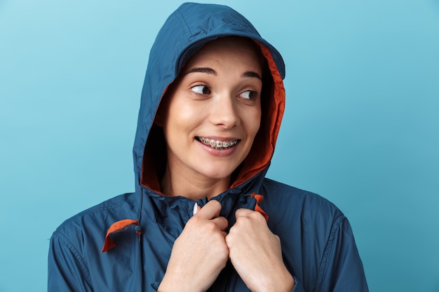 Joyeuse jeune fille portant un imperméable debout isolé sur un mur bleu, posant