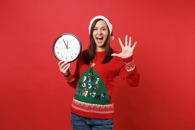 Joyeuse jeune fille de Santa tenant une horloge ronde montrant des doigts écartant la paume isolés sur fond rouge. Le temps presse. Bonne année 2019 concept de fête de vacances célébration. Maquette de l'espace de copie.