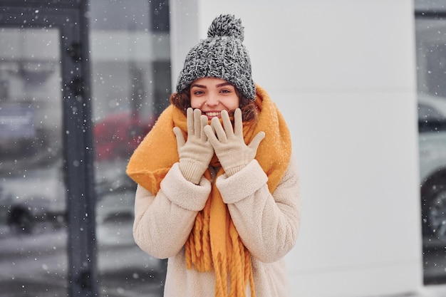 Joyeuse jeune fille souriante debout et souriante à l'extérieur. La neige est en train de tomber.