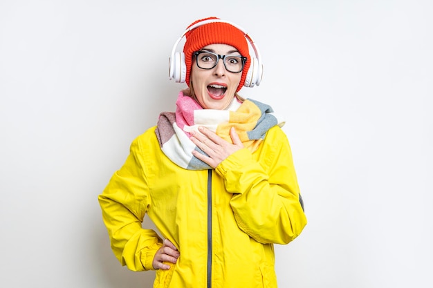 Joyeuse jeune fille surprise dans des écouteurs dans une veste jaune sur fond clair