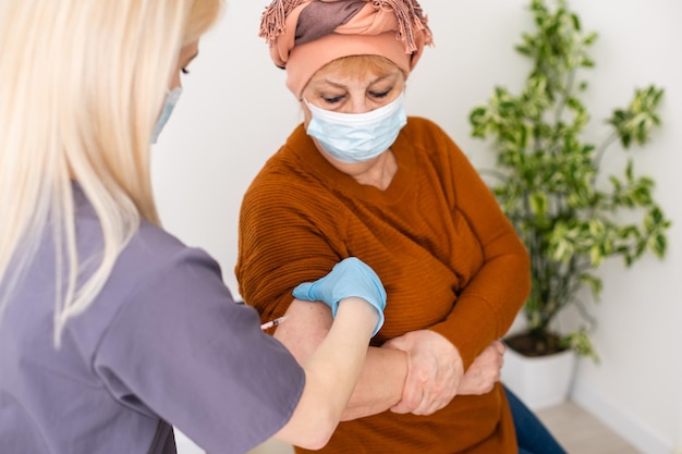 joyeuse jeune infirmière donnant une injection de vaccin à une femme âgée à la maison.