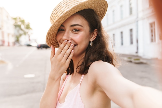 joyeuse jeune jolie femme au beau chapeau marchant dans la rue prendre selfie par caméra.