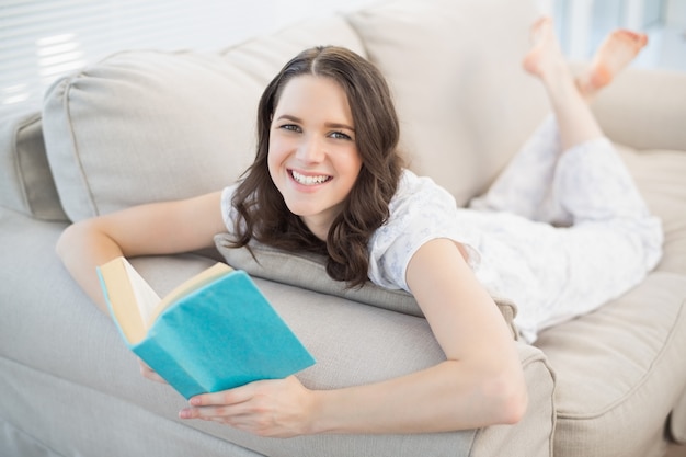 Joyeuse jolie femme allongée sur un canapé confortable lecture livre