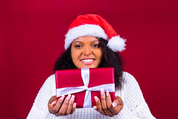 Joyeuse jolie femme en chapeau de père noël rouge riant isolé sur fond rouge elle est heureuse et excitée pleine de plaisir tenant une boîte cadeau