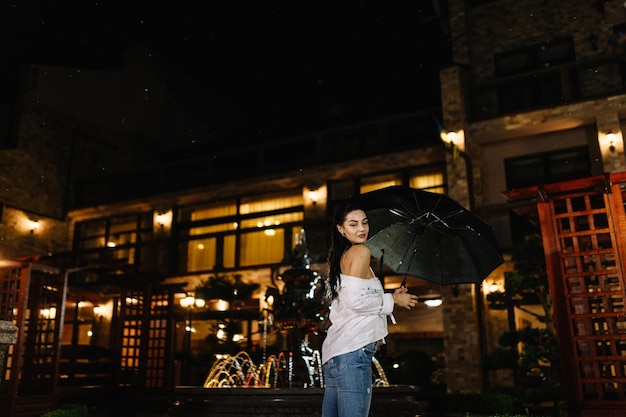 Joyeuse jolie fille tenant un parapluie en se promenant à l'extérieur Elle se retourne et regarde la caméra avec un vrai plaisir et un sourire sincère Copiez l'espace sur le côté droit