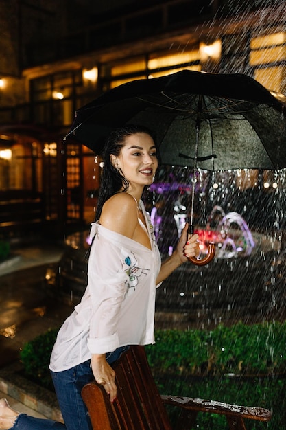 Joyeuse jolie fille tenant un parapluie en se promenant à l'extérieur Elle se retourne et regarde la caméra avec un vrai plaisir et un sourire sincère Copiez l'espace sur le côté droit