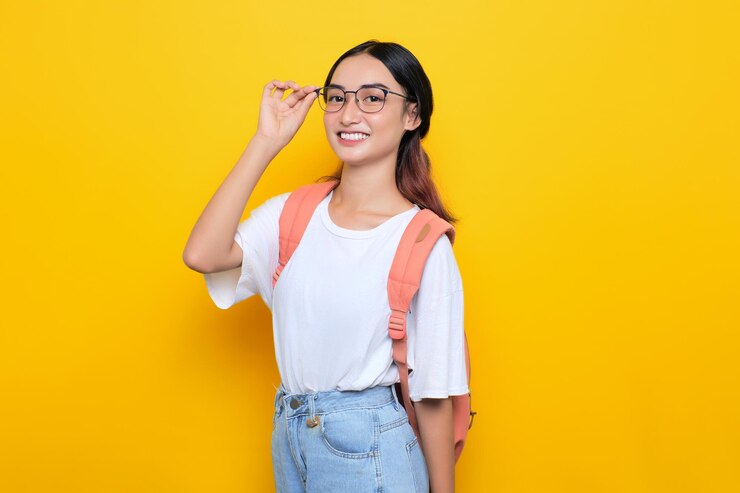 Joyeuse jolie jeune étudiante portant un sac à dos et des lunettes regardant la caméra isolée sur fond jaune