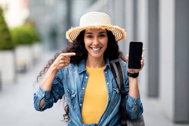 Joyeuse jolie touriste montrant un smartphone avec une maquette d'écran vide