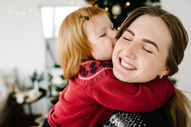 Joyeuse maman embrassant une jolie petite fille près de l'arbre de Noël Joyeux Noël et bonnes vacances