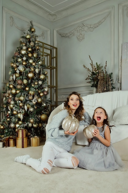 Joyeuse maman et sa jolie fille échangeant des cadeaux pour Joyeux Noël et Bonne Année. Mère et petit enfant s'amusant près de l'arbre de Noël à l'intérieur. Belle famille avec des cadeaux dans la chambre