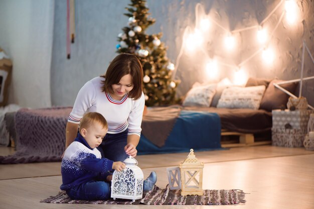 Joyeuse maman et son fils mignon s'amuser près de l'arbre à l'intérieur. Famille aimante dans la chambre de Noël.