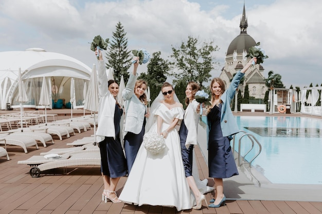 Joyeuse mariée et demoiselles d'honneur avec des bouquets posant à l'extérieur