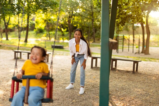 Photo joyeuse mère asiatique balançant sa petite fille sur une balançoire du parc à l'extérieur